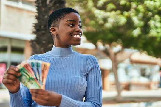 Young african american woman smiling happy counting south africa rand banknotes at the city.