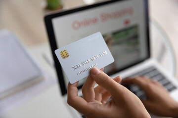 Modern tech usage, easy comfort e-shopping from home, secure electronic payment, cashback concept. Close up above view female hands holds credit card use laptop makes e-pay through e-bank application