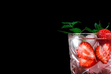 Strawberry alcoholic drink with liquor, ice cubes and mint in glass on black. Copy space