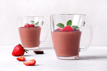 Chocolate mousse topped with strawberry and mint in irregular glass cup on the white table. Whipped exquisite dessert