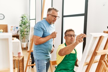 Fototapeta premium Group of middle age paint students drawing at art studio. Teacher with serious expression looking student draw.