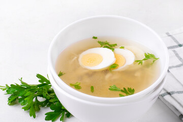 Chicken soup with vermicelli and boiled eggs topped with parsley served in the white bowl. Nutritious hot meal