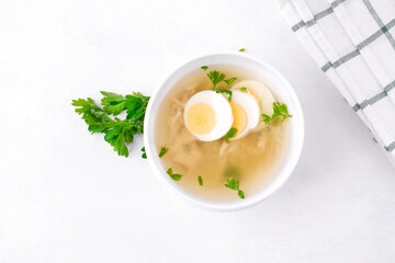Chicken soup with vermicelli and boiled eggs topped with parsley served in the white bowl. Nutritious hot meal. Top view