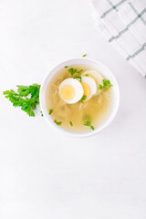 Chicken soup with vermicelli and boiled eggs topped with parsley served in the white bowl. Nutritious hot meal. Top view