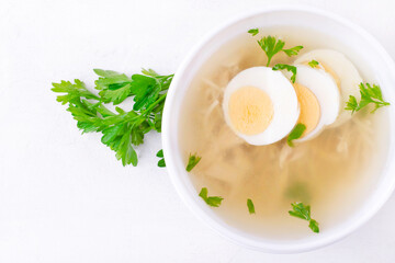 Chicken soup with vermicelli and boiled eggs topped with parsley served in the white bowl. Nutritious hot meal. Top view