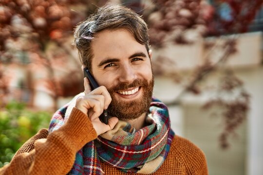 Caucasian man with beard having a conversation speaking on the phone outdoors on a sunny day