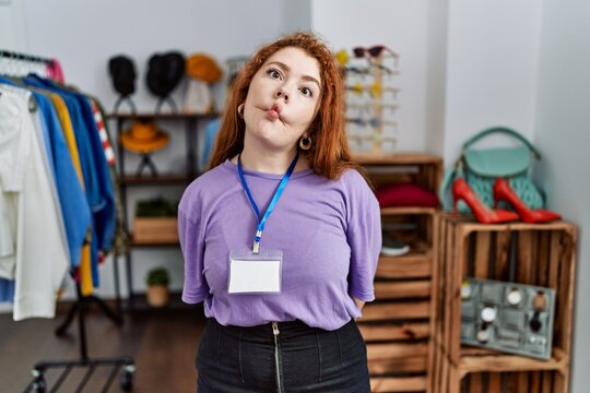 Young redhead woman working as manager at retail boutique making fish face with lips, crazy and comical gesture. funny expression.