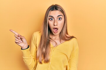 Fototapeta premium Beautiful hispanic woman wearing casual yellow sweater surprised pointing with finger to the side, open mouth amazed expression.