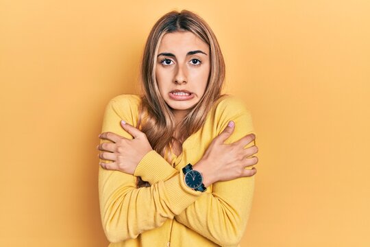 Beautiful hispanic woman wearing casual yellow sweater shaking and freezing for winter cold with sad and shock expression on face