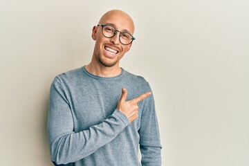 Bald man with beard wearing casual clothes and glasses smiling cheerful pointing with hand and finger up to the side