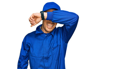 Bald man with beard wearing builder jumpsuit uniform covering eyes with arm smiling cheerful and funny. blind concept.