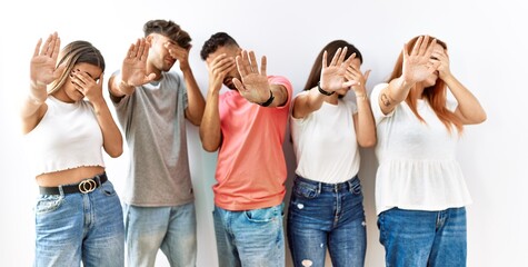 Fototapeta premium Group of young friends standing together over isolated background covering eyes with hands and doing stop gesture with sad and fear expression. embarrassed and negative concept.