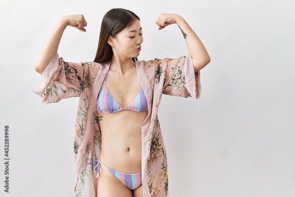 Poster Young asian woman wearing bikini an floral kimono showing arms muscles smiling proud. fitness concept.