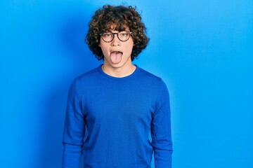Fototapeta na wymiar Handsome young man wearing casual clothes and glasses sticking tongue out happy with funny expression. emotion concept.