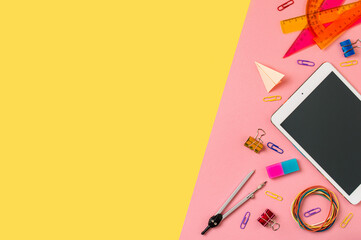 Creative student desk with tablet pc and colorful modern school supplies on yellow and pink duotone background. Top view. Flat lay. Copy space. Back to school concept