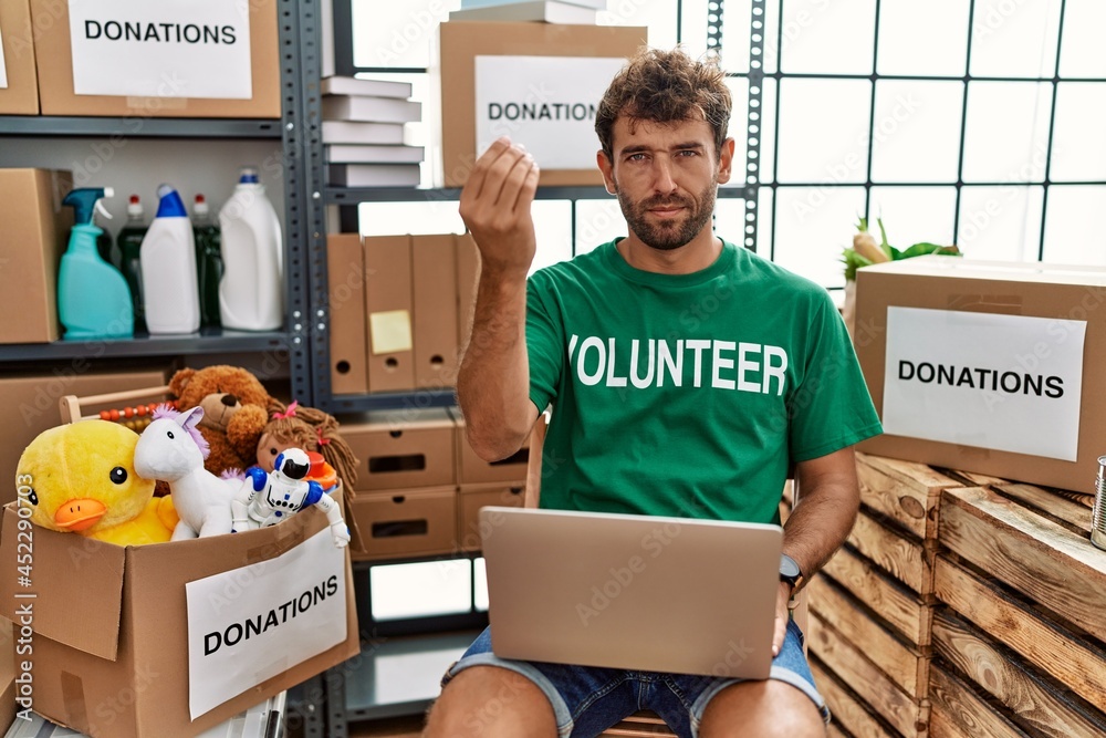 Wall mural young handsome man wearing volunteer t shirt using laptop doing italian gesture with hand and finger