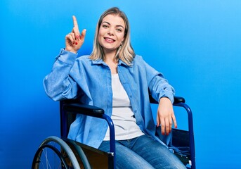 Beautiful caucasian woman sitting on wheelchair showing and pointing up with finger number one while smiling confident and happy.