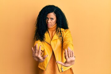 Middle age african american woman wearing wool winter sweater and leather jacket doing stop gesture with hands palms, angry and frustration expression