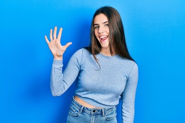 Fototapeta na wymiar Young brunette teenager wearing casual sweater showing and pointing up with fingers number five while smiling confident and happy.