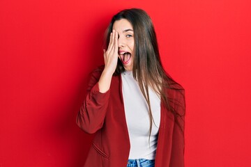 Young brunette teenager wearing business jacket covering one eye with hand, confident smile on face and surprise emotion.