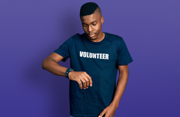 Young african american man wearing volunteer t shirt checking the time on wrist watch, relaxed and confident
