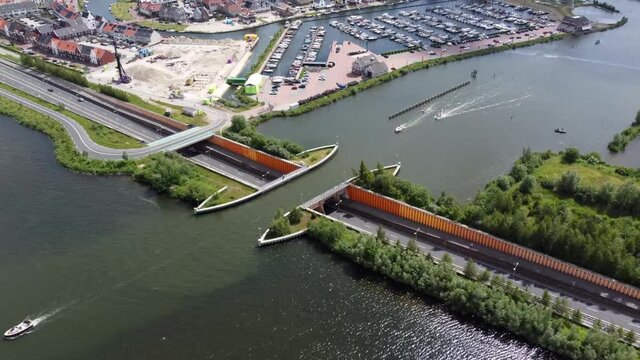 Aerial drone view of aqueduct or water bridge constructed to convey watercourses across gaps showing recreational boats moving towards the infrastructure and traffic going underneath it 4k quality