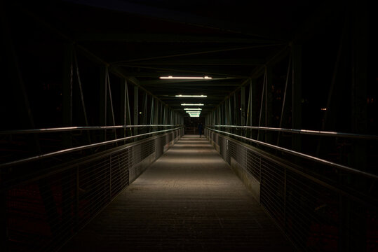 A nightly photographed bridge in an nostalgic look with a person walking far at the end of the bridge