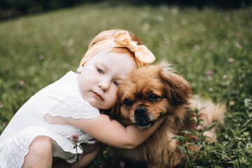 Cute red headed girl with her red haired dog in the summer park. Child and the pet. Little friend.