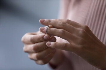 Unrecognizable young woman takes off wedding ring, remove engagement jewellery as sign of divorcement, close up cropped view. Break up, cheated wife, infidelity, marriage end, relations split concept - obrazy, fototapety, plakaty