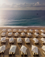 aerial view of an amazing empty white beach with white beach umbrellas and turquoise clear water during the sunrise. Mediterranean sea.