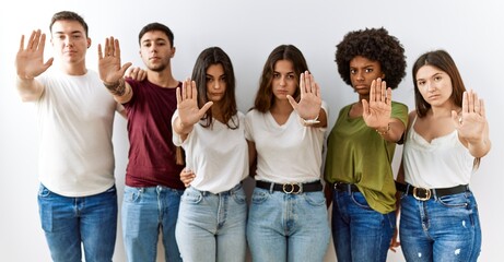 Group of young friends standing together over isolated background doing stop sing with palm of the...