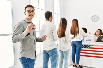 Group of young american voter people putting vote in ballot. Man smiling happy and holding i voted badge at electoral center. - obrazy, fototapety, plakaty