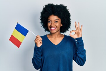 Young african american woman holding romania flag doing ok sign with fingers, smiling friendly gesturing excellent symbol