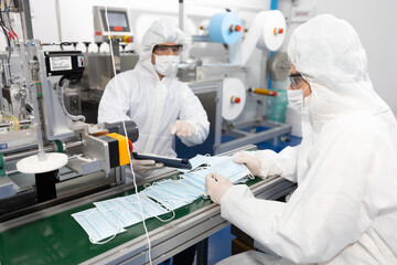 male engineers wearing personal protective equipment uniform(PPE), producing medical face mask beside machine in laboratory