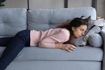 Exhausted young woman lying on sofa sleeping at end of hard workday, after hard-working day. Tired female fall asleep on couch face in cushion. Fatigue relief, no motivation, sleepless night concept - obrazy, fototapety, plakaty
