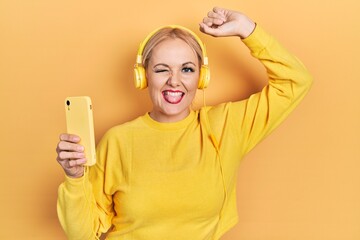 Young blonde woman dancing wearing headphones sticking tongue out happy with funny expression.