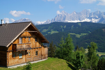 Fototapeta na wymiar scenic alpine panorama with an alpine log cabin and Dachstein mountain in the background in the Austrian Alps of the Schladming-Dachstein region (Almwelt Austria (Reiteralm Chalets))