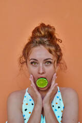 Ginger woman playing with lime on orange background