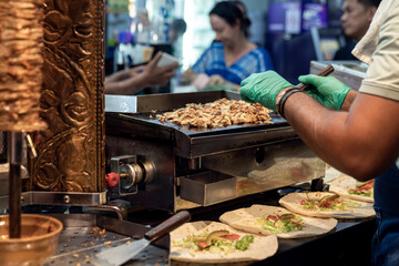 a male chef prepares a meat shawarma on the street. He puts fried meat in tortillas. the cook's...