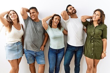 Group of young hispanic friends standing together over isolated background smiling confident touching hair with hand up gesture, posing attractive and fashionable