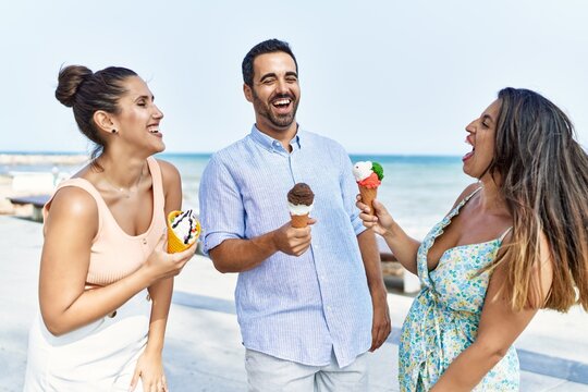 Three young hispanic friends smiling happy eating ice cream at the beach.