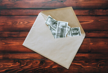 A large craft beige envelope with dollar bills lies on a brown table. The concept of a bribe, donation, alimony. View from above.
