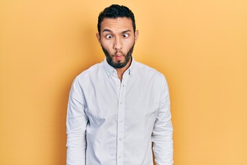 Hispanic man with beard wearing business shirt making fish face with lips, crazy and comical gesture. funny expression.