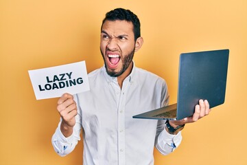 Hispanic man with beard working using computer laptop holding lazy loading banner angry and mad screaming frustrated and furious, shouting with anger. rage and aggressive concept.