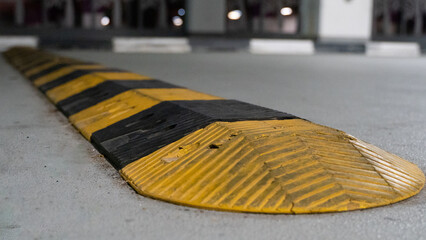 Traffic safety speed bump on an asphalt road in a parking area. Speed bumps (or speed breakers) are...