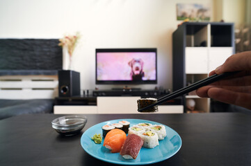 first person view of hand picking up a piece of sushi with chopsticks against an out-of-focus...