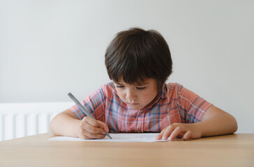 Naklejka premium Schoolboy using pencil drawing on white paper sheet, Young kid doing school homework, Happy mixed race child enjoy doing arts and crafts at home on weekend. Home schooling, Education concept