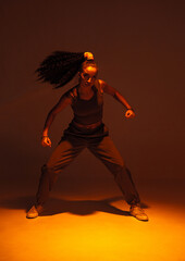 Dancing athletic mixed race girl performing expressive fiery hip hop or ethnic african modern dance in warm studio light