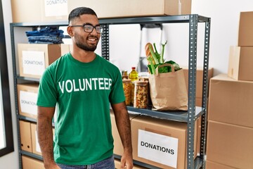 Young indian man volunteer holding donations box looking away to side with smile on face, natural expression. laughing confident.