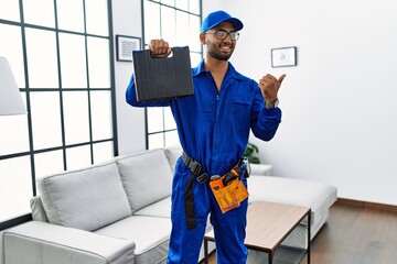 Young indian technician holding toolbox and screwdriver at house pointing thumb up to the side smiling happy with open mouth